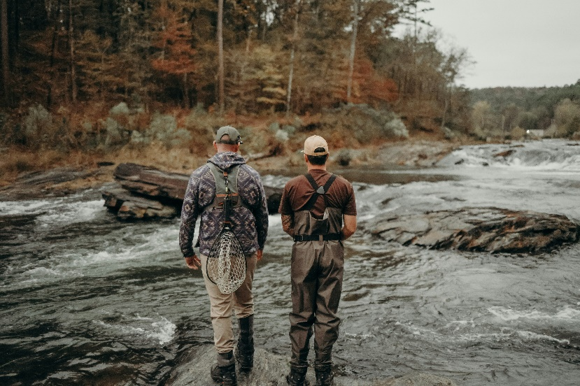 Couple standing on rocks above a river surrounded by trees.